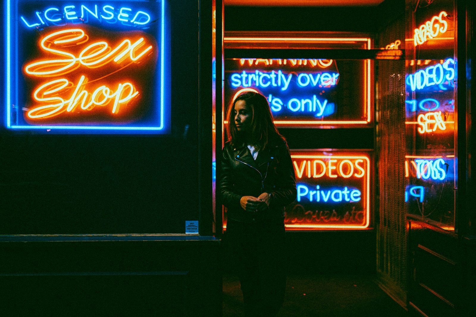 woman in black jacket standing in front of blue and red UNKs neon signage